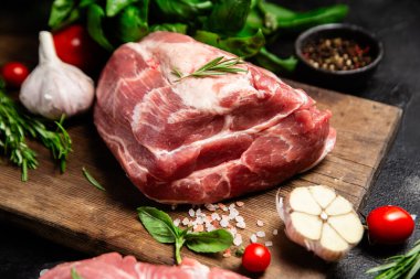 Ahşap bir tahtada çiğ domuz eti, otlar ve domateslerle pişirilmeye hazır.