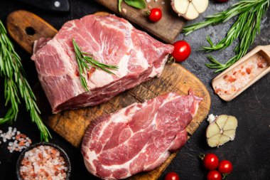 Ahşap bir tahtada çiğ domuz eti, otlar ve domateslerle pişirilmeye hazır.