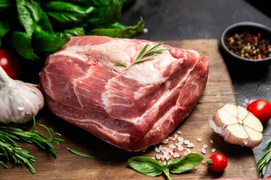 Ahşap bir tahtada çiğ domuz eti, otlar ve domateslerle pişirilmeye hazır.