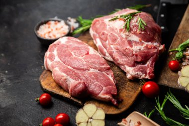 Ahşap bir tahtada çiğ domuz eti, otlar ve domateslerle pişirilmeye hazır.