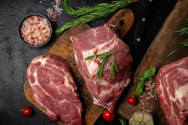 Ahşap bir tahtada çiğ domuz eti, otlar ve domateslerle pişirilmeye hazır.