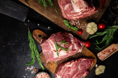 Ahşap bir tahtada çiğ domuz eti, otlar ve domateslerle pişirilmeye hazır.