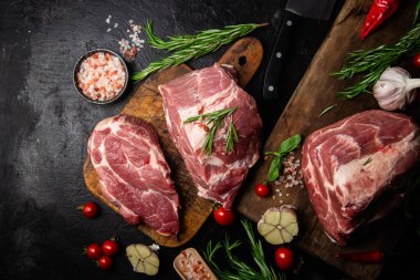 Ahşap bir tahtada çiğ domuz eti, otlar ve domateslerle pişirilmeye hazır.