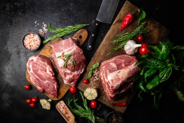 Ahşap bir tahtada çiğ domuz eti, otlar ve domateslerle pişirilmeye hazır.