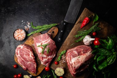 Ahşap bir tahtada çiğ domuz eti, otlar ve domateslerle pişirilmeye hazır.