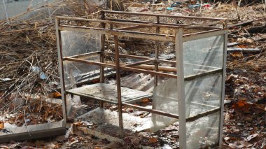 Terk edilmiş bir cam vitrin, kuru yapraklar ve molozlarla çevrili terk edilmiş bir alanda duruyor. Çürüme ve unutulmuş anılar hissi uyandırıyor.