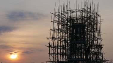 Gün batımında gökyüzüne karşı iskelesi olan bir inşaat alanı silueti iskelenin karmaşık yapısını gözler önüne seriyor. Sahne gelişim ve gelişim duygusunu çağrıştırıyor