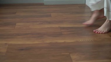 Ahşap zeminde insan ayağı. Genç kadın çıplak ayakla odada daireler çiziyor ve dans ediyor. Beyaz pantolonlu bir kadın. Tanınmayan kızın bacakları..