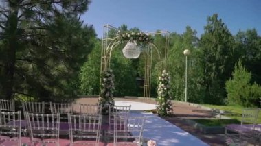 Çiçek ve sandalyeli düğün kemeri. Seremoni salonu açık havada. Beyaz çiçekler ve yeşilliklerle süslenmiş. Güneşli yaz günü.