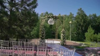 Çiçek ve sandalyeli düğün kemeri. Seremoni salonu açık havada. Beyaz çiçekler ve yeşilliklerle süslenmiş. Güneşli yaz günü.