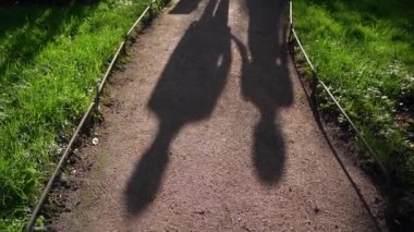 Gelin ve damat toprak yolda yürüyor. Düğün çifti parkta yürüyor. Güneşli bir günde insanların gölgeleri. Gelinlik, millet. Aşk, romantik.