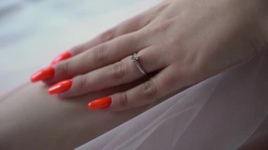 Gelin elleriyle bacağına dokunuyor. Parmağında yüzük var. Beyaz gelinlik ya da peçeyle baştan çıkarıcı hareket eden genç kadın..