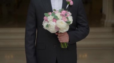 Siyah bir takım elbise içinde bir buket beyaz ve pembe gül ve kurdeleli şakayıklar. Bir erkek işadamı, aşk kadınına bir hediye taşır. Romantik bir gün..