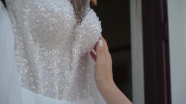 Kadın elinde askıda beyaz bir gelinlik tutuyor. Gelinin sabahı, giyiniyor.