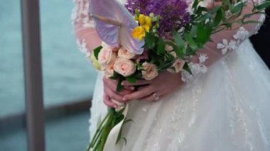 Bir göl düğünü töreninde, güzel bir gelin elinde zarif bir buket gül, anthurium ve diğer çiçek süslemeleriyle yakından görülür. Bu etkinlik sevgi ve gelenekle dolu.