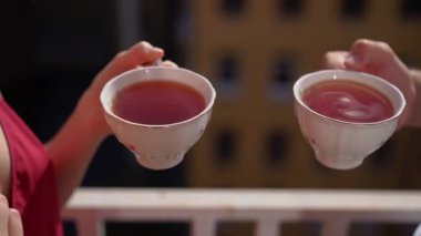 İki fincan çay. Genç bir çift elinde sıcak içecekle fincanla çay ya da kahve tutuyor. Erkek ve kadın yaz sabahı balkonda içiyorlar. Tatilde kahvaltı ediyorlar..