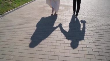 Gelin ve damat toprak yolda yürüyor. Düğün çifti parkta yürüyor. Güneşli bir günde insanların gölgeleri. Gelinlik, millet. Aşk, romantik.