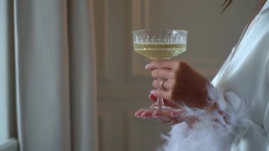 Genç bir kadın kristal bardağı beyaz şarapla alır ve tutar. Kız şampanya içiyor. Beyaz bornozlu bir kadın, tatilde bir sabah kahvaltı yapar..