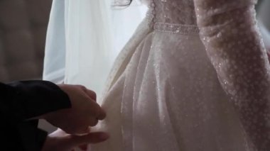 Gelin bir gelinlik giyiyor. Sabahleyin beyaz dantelli, lüks elbiseli genç bir kız. Nedime ya da anne korsenin arkasına fermuarını çeker..