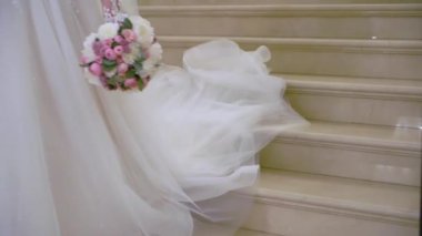 Beyaz gelinlik giymiş genç bir kadın merdivenle aşağı iniyor. Bacaklar topuklu ayakkabılar, elbise ve çiçek buketi..