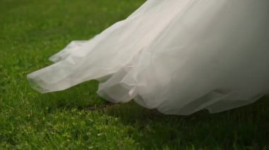 Uzun beyaz bir gelinlik ve yüksek topuklu ayakkabılar içinde çimlerde yürüyen bir gelin. Düğün töreni, resepsiyon. Kadın ağır ağır kaçıyor..