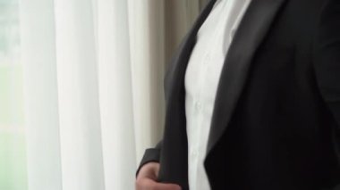 Takım elbisenin düğmelerini ilikleyen ellerin yakın çekimi. Adam siyah ceket giydi. Düğün günü damat ya da iş adamı. Beyaz gömlekli bir erkek..