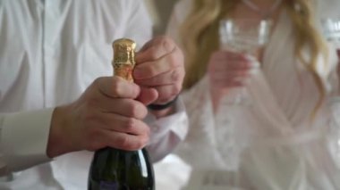 Adam şampanyadan bardaklara şampanya dolduruyor. Beyaz köpüklü alkollü şarap içeceği. Romantik randevu tatilindeki çift, erkek ve genç kadın..