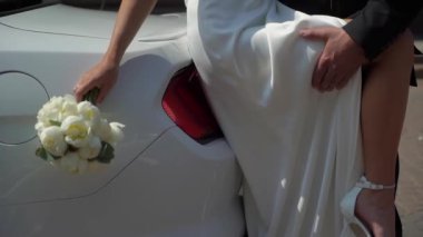 Gelin ve damat sarılıyor. Beyaz gelinlikli, duvağı ve klasik takım elbisesi olan genç bir çift. Karı koca, ilişki, aile, evlilik yıldönümü ya da balayı. Beyaz araba.
