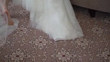 Kadın elinde askıda beyaz bir gelinlik tutuyor. Gelinin sabahı, giyiniyor.