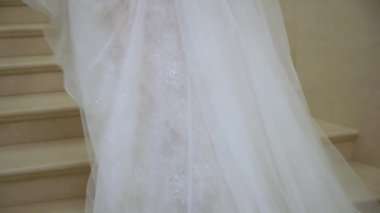 Beyaz gelinlik içindeki genç kadın merdivenlerden yukarı çıkıyor. Bacaklar topuklu ayakkabılar, elbise ve çiçek buketi..