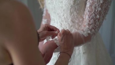 Gelin, zarif dantelli elbiseyi dikkatlice bağlarken özel bir ilgi gösteriyor. Güzel ve içten bir düğün töreni için güzel anılar yaratıyor.