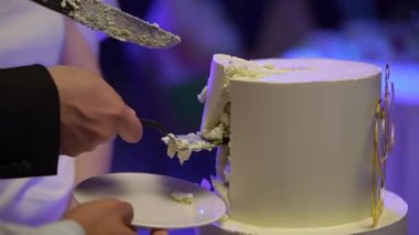 Kutlama pastası kesen biri. Gelin ve damat düğün resepsiyonunda. Bıçak tutan adam ve kadın bir dilim tatlı kestiler..