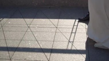 Gelin ve damat kaldırımda yürürler. Erkek ve kadın bacakları, düğün çifti. Beyaz uzun elbiseli kız..