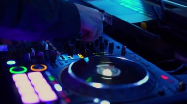 Bir DJ 'in elleri canlı bir karıştırma konsolu üzerinde, renkli tuşları ve pikapları vurguluyor, müzik ve gece hayatı temaları için mükemmel.