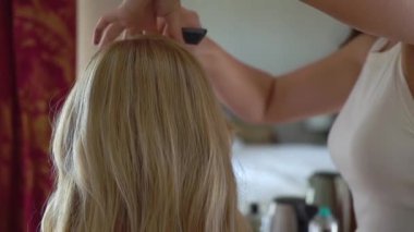 Hairdresser makes the girls hair with a electric curling iron. Unrecognizable caucasian woman curls her hair, styling. Preparing for the holiday.