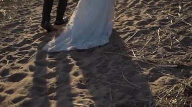 Genç ve romantik bir çift akşam güneşinde kumsalda yürüyor. Erkek ve kadın el ele tutuşup sarılıyor. Kız yalınayak kuma gider. Gelin ve damat beyaz elbise ve takım elbiseleriyle düğünlerinde..