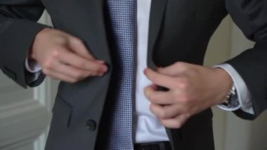 Takım elbisenin düğmelerini ilikleyen ellerin yakın çekimi. Adam siyah ceket giydi. Düğün günü damat ya da iş adamı. Beyaz gömlekli bir erkek..