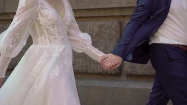 Gelin ve damat kaldırımda yürürler. Erkek ve kadın bacakları, düğün çifti. Beyaz uzun elbiseli kız..