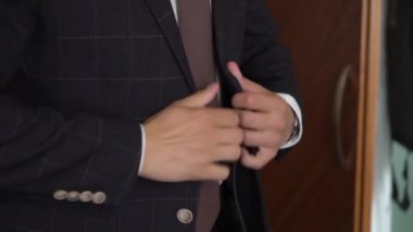 Takım elbisenin düğmelerini ilikleyen ellerin yakın çekimi. Adam siyah ceket giydi. Düğün günü damat ya da iş adamı. Beyaz gömlekli bir erkek..