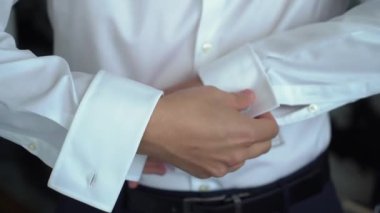 Gömleğinin düğmelerini ilikleyen, beyaz gömlek ve kol düğmeleri takan bir adam. Kişi beyaz gömlek ve kol düğmesi takıyor. Damat düğüne gidiyor..