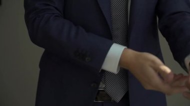 Takım elbisenin düğmelerini ilikleyen ellerin yakın çekimi. Adam siyah ceket giydi. Düğün günü damat ya da iş adamı. Beyaz gömlekli bir erkek..