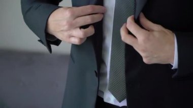 Takım elbisenin düğmelerini ilikleyen ellerin yakın çekimi. Adam siyah ceket giydi. Düğün günü damat ya da iş adamı. Beyaz gömlekli bir erkek..