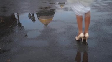 Gelin ve damat kaldırımda yürürler. Erkek ve kadın bacakları, düğün çifti. Beyaz uzun elbiseli kız. Koş ve bir su birikintisinin üzerinden atla..