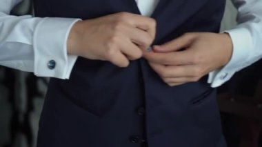 Bir adam cekete ya da yeleğe düğme takıyor. Erkek klasik bir takım elbise giyer. İş adamı, ofis çalışanı ya da damat..