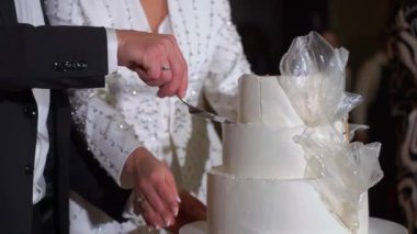 Kutlama pastası kesen biri. Gelin ve damat düğün resepsiyonunda. Bıçak tutan adam ve kadın bir dilim tatlı kestiler..