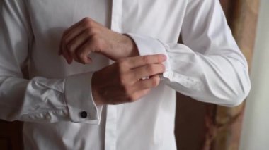 Gömleğinin düğmelerini ilikleyen, beyaz gömlek ve kol düğmeleri takan bir adam. Kişi beyaz gömlek ve kol düğmesi takıyor. Damat düğüne gidiyor..