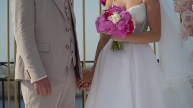 Gelin ve damat el ele tutuşuyor. Beyaz gelinlikli genç bir kadın ve takım elbiseli bir adam. Sevgi, ilgi ve şefkat. Birlikte.