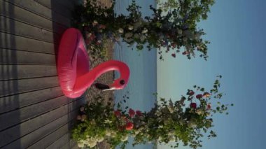 Çiçek ve sandalyeli düğün kemeri. Seremoni salonu açık havada. Beyaz çiçekler ve yeşilliklerle süslenmiş. Güneşli bir yaz günü. Pembe şişirilebilir flamingo.. 