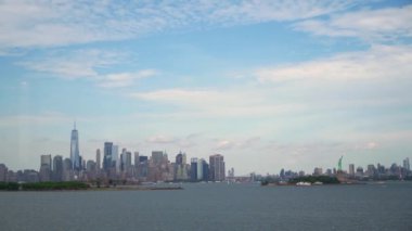 New York şehrinin ufuk çizgisi, bu ikonik şehrin güzelliğini sergileyen, parçalı bulutlu gökyüzünün altında görülen One World Ticaret Merkezi ve Hudson Nehri ile nefes kesici bir manzara sunuyor.