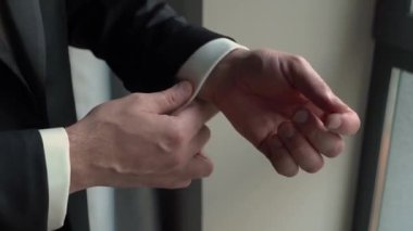 Kendinden emin bir adam parlayan kol düğmelerini ayarlar, resmi kıyafetlerini ve detaylara olan ilgisini gösterir.